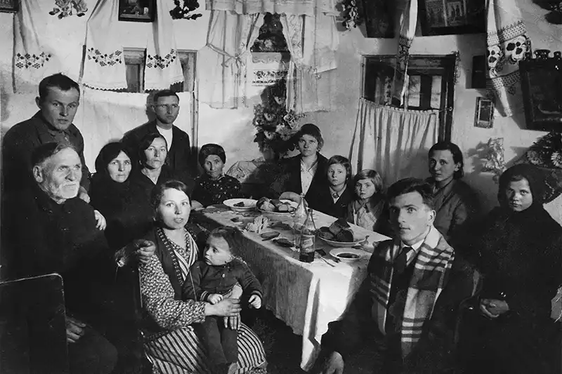 Een zwart-wit foto van een groot gezin en meerdere generaties aan één tafel.