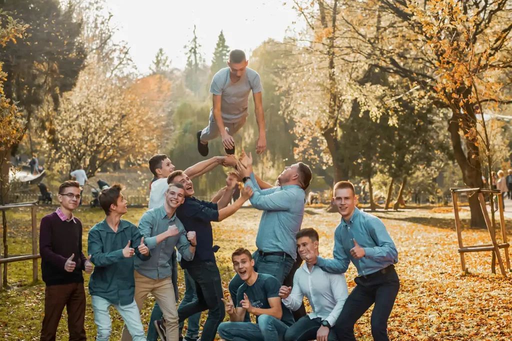 Een groep jonge mannen in een park die samen één jongen uit de groep de lucht in gooien en weer opvangen.