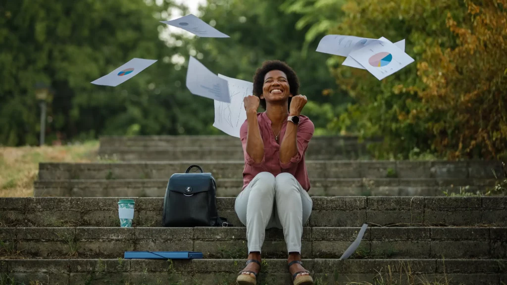Zakenvrouw op de trap met gesloten ogen, een grijns en vuisten gebald omhoog Om haar heen dwarrelen in de lucht gegooide papieren met schema's terug naar de grond.